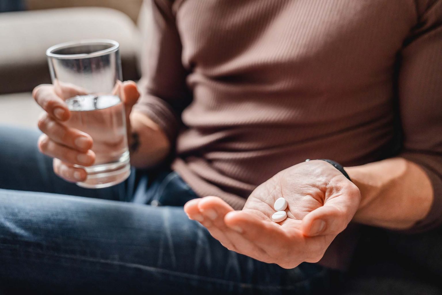 Person with glass of water and aspirin in hand