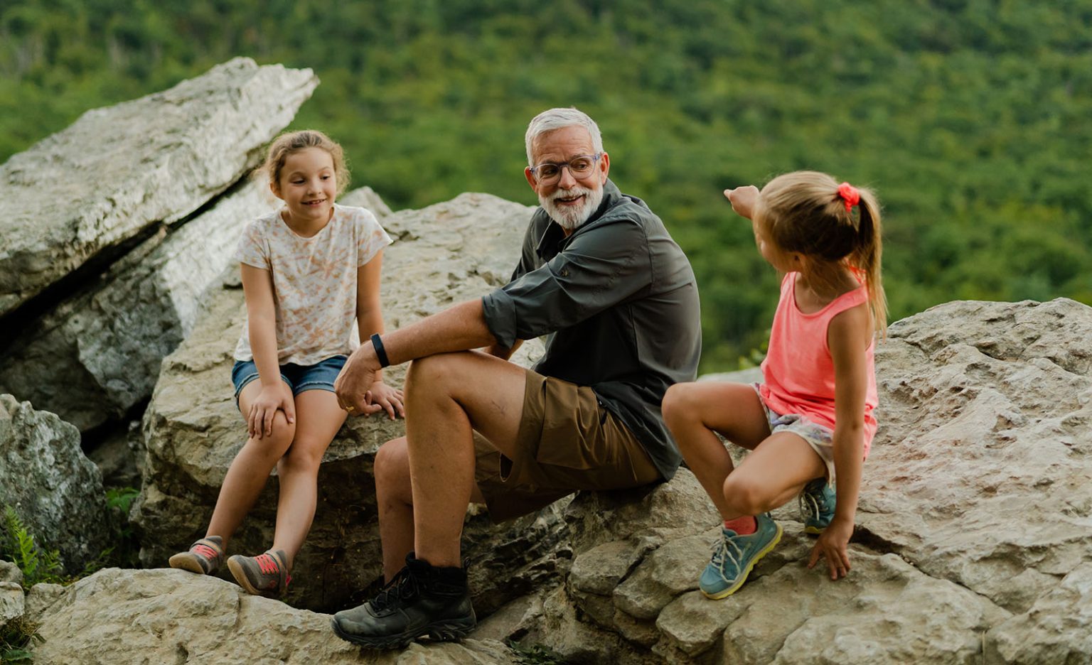 John and his granddaughters sitting on rocks during hike.