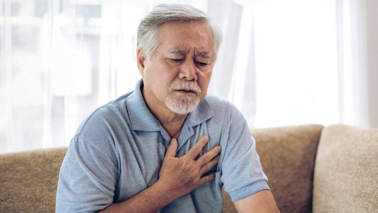 A senior Asian man placing his hand over his chest while at home.