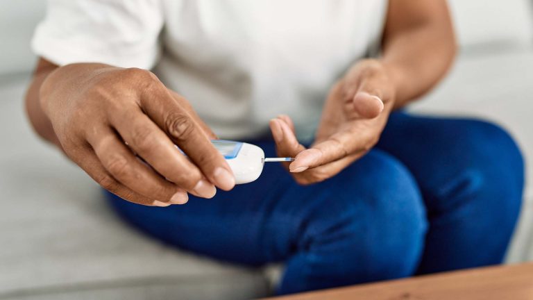 Senior African American woman measuring glucose at home.