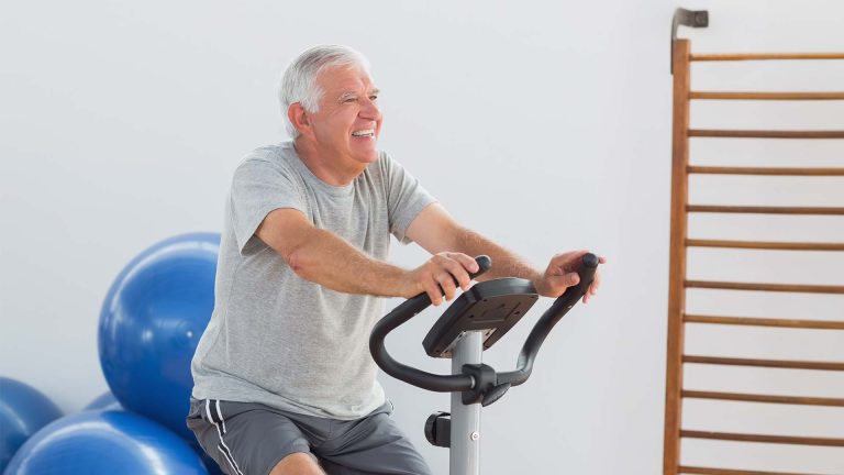 Smiling senior man exercising on fitness bike.