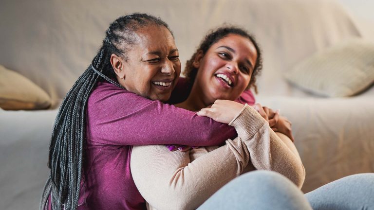 Happy mother and adult daughter hugging each other after yoga class at home.