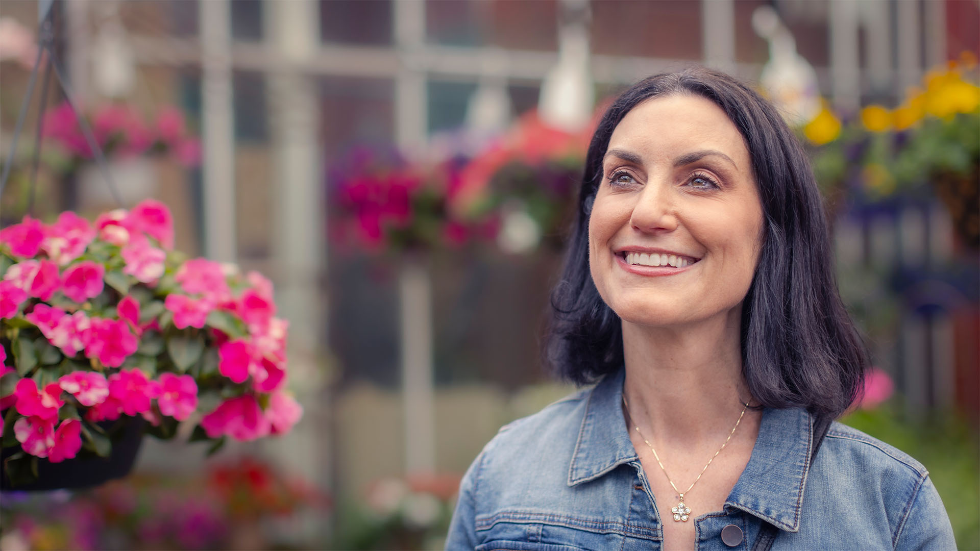 Alexis smiling in greenhouse with pink flowers.