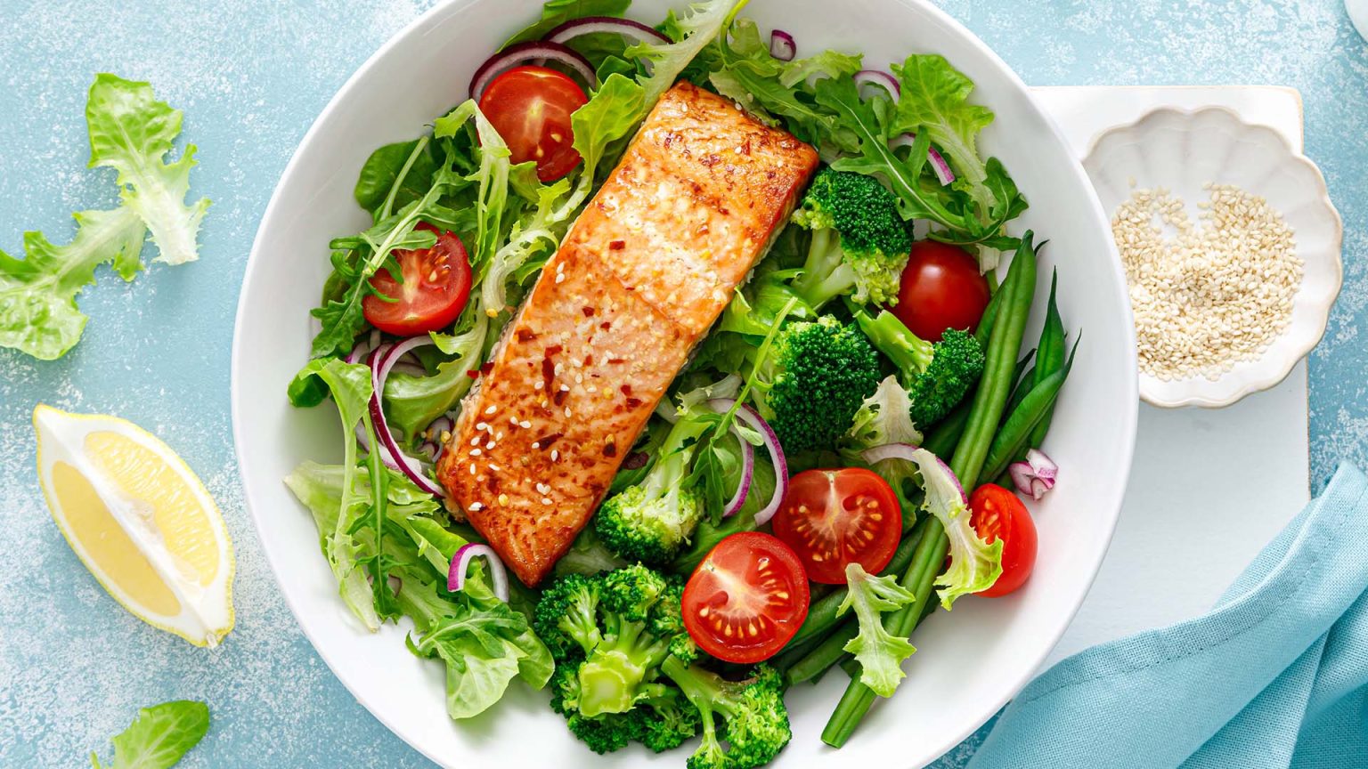 Grilled salmon fish fillet and fresh tomato vegetable salad with lettuce, arugula, broccoli and green beans.