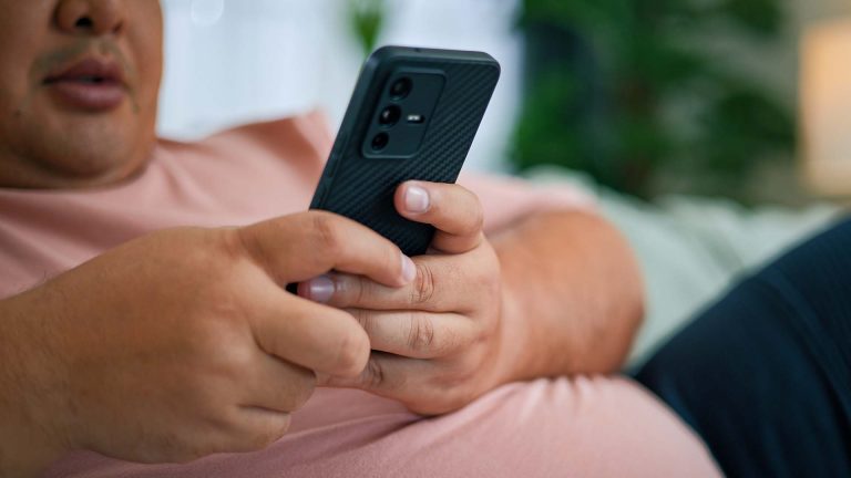 Chubby man using smartphone relaxing on sofa in living room