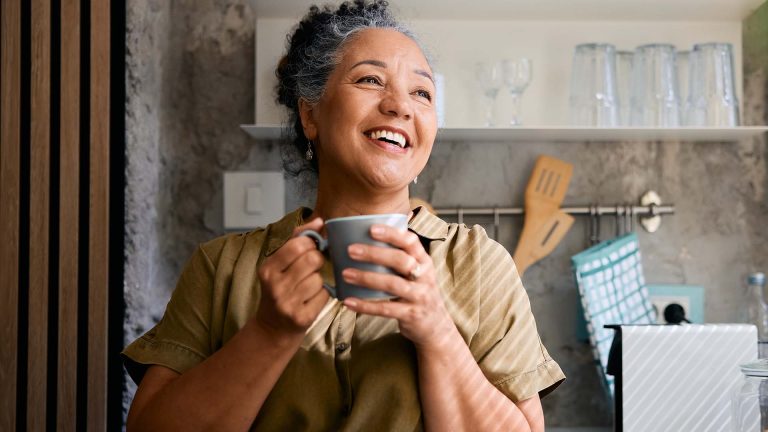 Smiling woman holding a cup of coffee in a cozy kitchen.